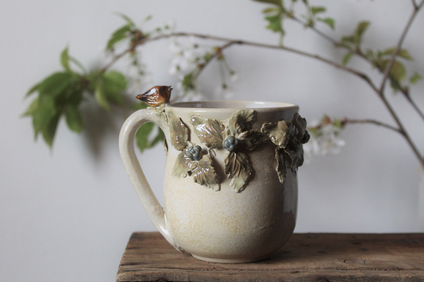 Tazza in gres color crema con uccellino sul manico e rami di more, fatta a mano al tornio