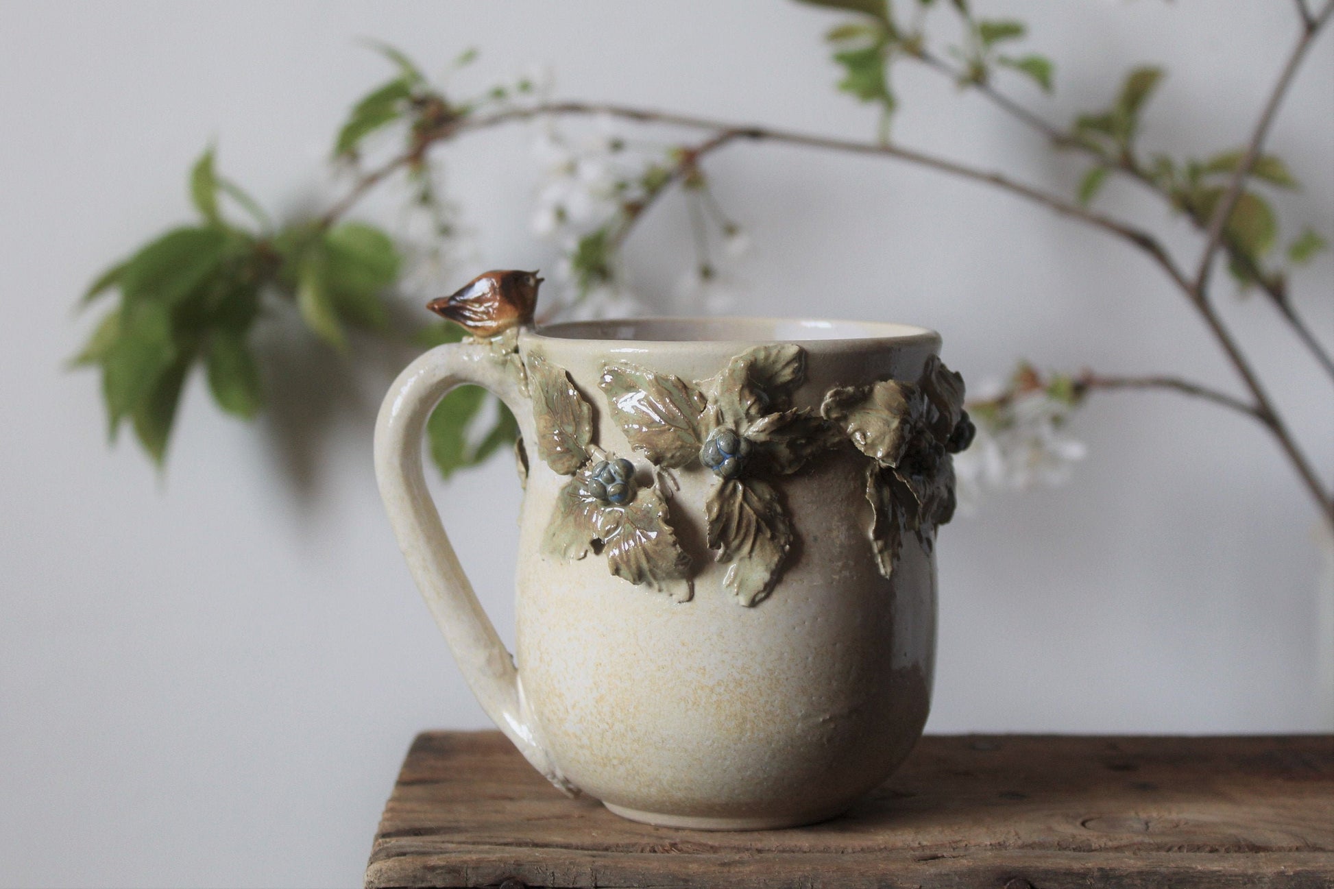 Tazza in gres color crema con uccellino sul manico e rami di more, fatta a mano al tornio
